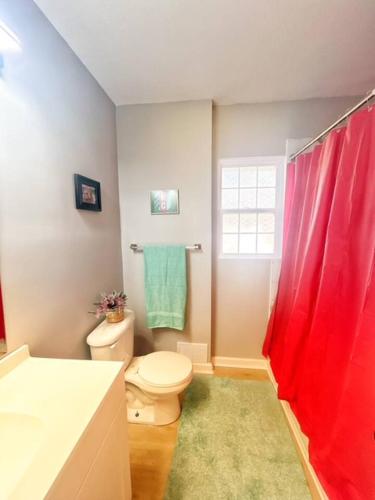 a bathroom with a toilet and a red shower curtain at Triple Crown KC in Kansas City
