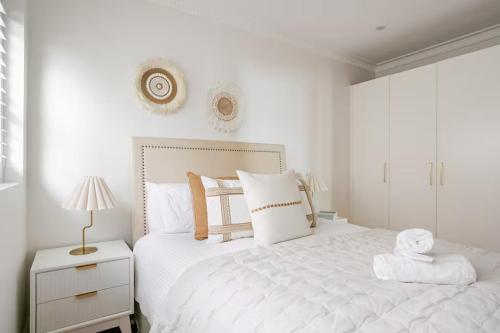 a white bedroom with a white bed and a lamp at Manly Beachfront Stays - 3 Bedroom with Garden - Steps to Ferry, Beach, Shops & Restaurants in Sydney