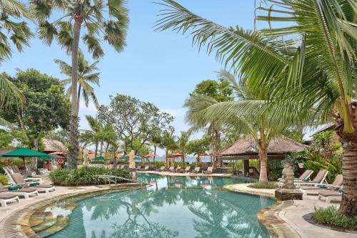 a pool at a resort with chairs and palm trees at Legian Beach Hotel in Legian