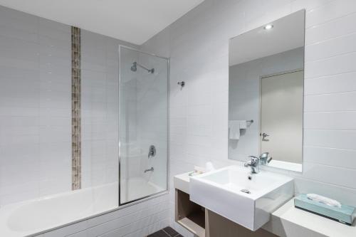 ein weißes Badezimmer mit einem Waschbecken und einem Spiegel in der Unterkunft Hunter Gateway Motel in Maitland