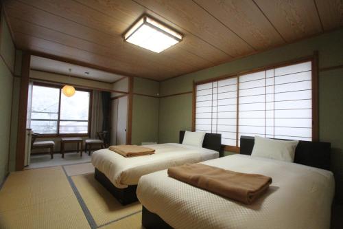 a bedroom with two beds in a room with windows at Hotel Hirayunomori Annex in Takayama