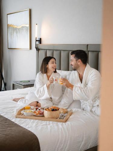a man and woman sitting on a bed eating food at Copthorne Hotel Sharjah in Sharjah