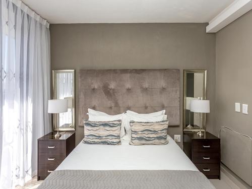 a bedroom with a large white bed with two lamps at Infinity Self Catering Apartments in Bloubergstrand