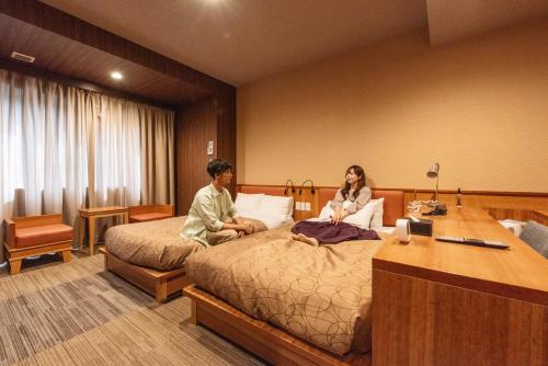 a man and woman sitting on a bed in a hotel room at HOTEL RELIEF Sapporo Susukino in Sapporo