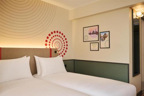 a bedroom with two white beds and a wall with art at iStay by NH Berlin City Ost Hotel in Berlin