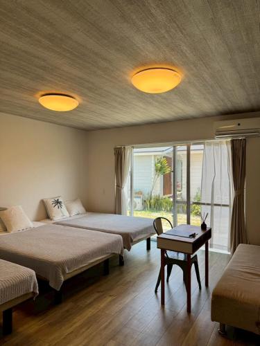 a bedroom with two beds and a table and a window at GuesthouseKAZE in Miyako-jima