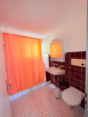 a bathroom with an orange shower curtain and a toilet at Haus Bünten in Quinten