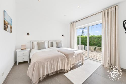 a white bedroom with a bed and a large window at Villa Benjamin - Vale do Lobo in Vale do Lobo
