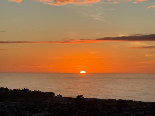 a sunset over the ocean with the sun in the sky at Panoramic Sea & Town View Oamaru 睁眼即见太平洋 I 躺观日月同辉 in Oamaru