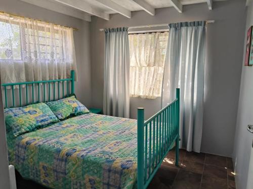 a green bed in a bedroom with windows at Sea Wave Cottage in Pearly Beach