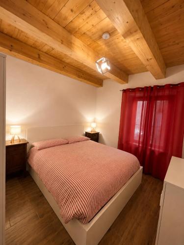 a bedroom with a bed with red curtains and wooden ceilings at Al Vagone in La Salle