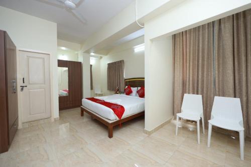 a bedroom with a bed and two white chairs at Hotel Amulya Relax Inn in Bangalore
