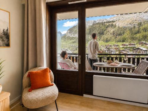 a man and a woman standing on a balcony looking out the window at Lodge Montëva - Le Chinaillon - Au pied des pistes in Le Grand-Bornand