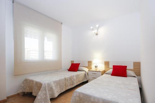 two beds with red pillows in a white room at Los Juncos HomeStay by Turismar in La Pineda