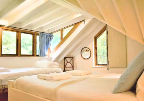 a attic bedroom with two beds and windows at Rural Cottage Retreat, Near Goodwood Festival of Speed, Dog Friendly with Shared Outdoor Pool, gardens & Tennis, Free Parking! Chichester Holiday Properties in North Mundham