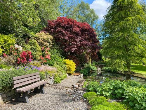 a park bench in a garden with flowers and a pond at Forge Mill Cottage in Dalbeattie