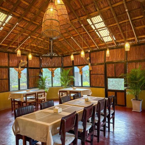 a dining room with tables and chairs and windows at Hotel Tharu Garden in Sauraha