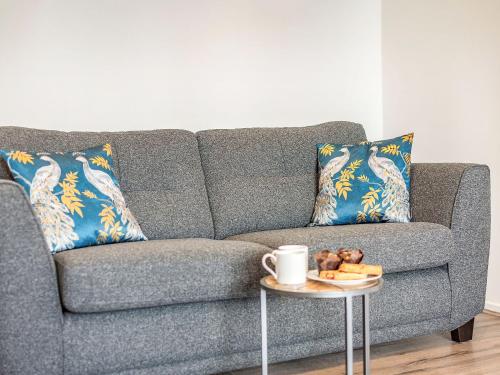 a gray couch with blue pillows and a table with a coffee cup at Hotspur View in Alnwick