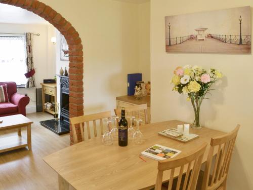 a dining room with a table with a bottle of wine and flowers at Watchkeeper's Cottage in Mundesley