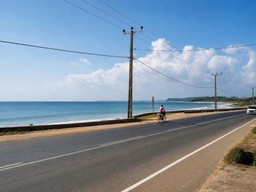 a person riding a bike down a road next to the ocean at Villa Yuvin in Matara