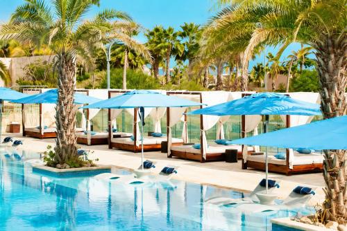a pool with blue umbrellas and chairs and palm trees at Palmilla Dunes Luxury Residences in San José del Cabo