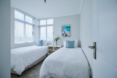 two beds in a white room with two windows at 2 Bedroom Bloubergstrand Apartment with Ocean Views in Bloubergstrand