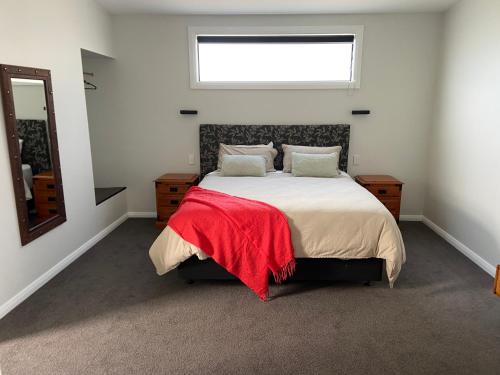 a bedroom with a bed with a red blanket on it at The Jam Shed in Waimate
