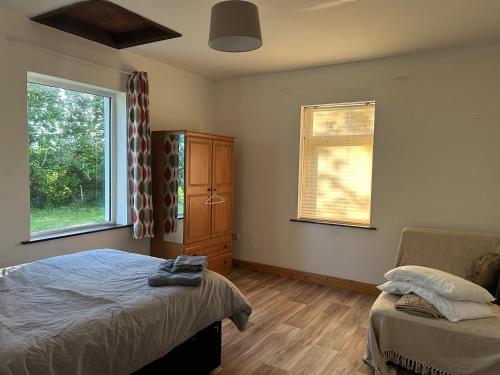 a bedroom with a bed and a chair and two windows at Ciaran's cottage in Donore