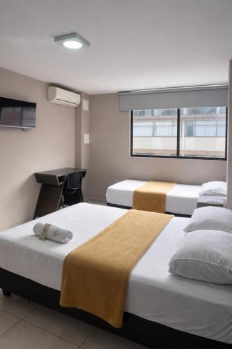 a room with three beds and a desk and a window at Hotel Escorial Ibagué in Ibagué