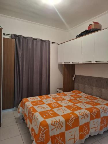 a bedroom with a bed with an orange and white blanket at Casa aconchegante in Peruíbe