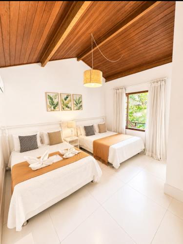 two beds in a white room with a wooden ceiling at Pousada Coisa e Tao in Arraial d'Ajuda
