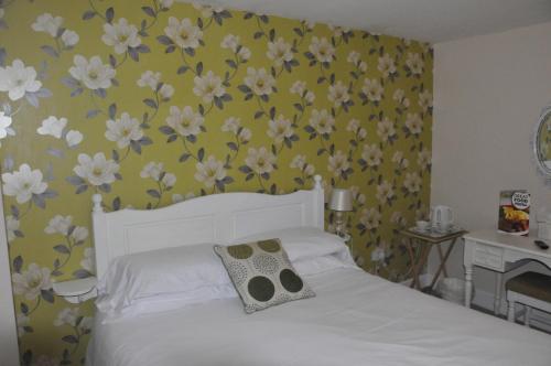 ein Schlafzimmer mit einem weißen Bett mit Blumen an der Wand in der Unterkunft The Sydney Arms in Dorchester