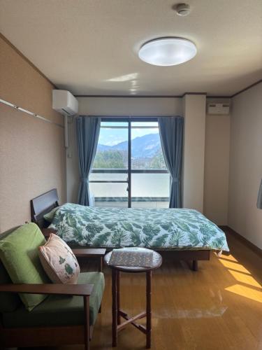 a bedroom with a bed and a chair and a window at サザンヒルズガーデン in Fujikawaguchiko