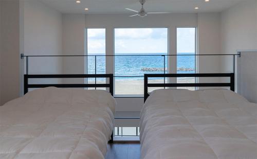 two beds in a bedroom with a view of the ocean at Tabinoteitaku Y-beach in Tsuruoka