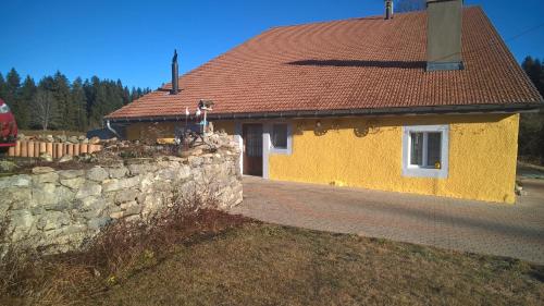 a yellow house with a red roof and a stone wall at La Dernier (La cote-aux-fées) Suisse in La Côte-aux-Fées