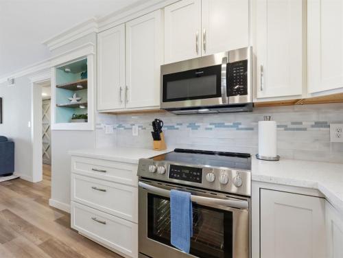 a kitchen with white cabinets and a stove and microwave at Kingfisher Oceanfront Condo w Pool & Elevator in North Topsail Beach