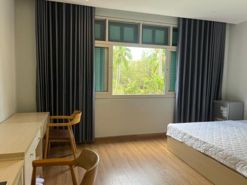a bedroom with a bed and a desk and a window at Emerald Marina TL in Phú Quốc