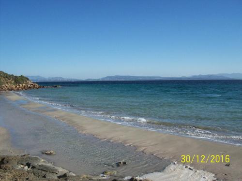 a sandy beach with the ocean and mountains in the background at Domos Le Due Tuie in Piscinas