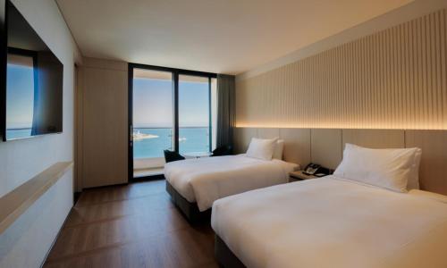two beds in a hotel room with a view of the ocean at Ulsan Tanibay Hotel & Wedding in Ulsan