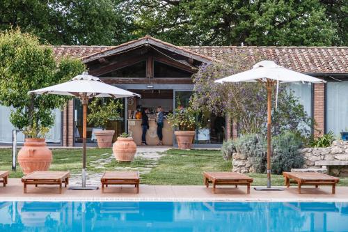 two umbrellas and benches next to a swimming pool at Villa Acquaviva Wine Resort in Montemerano