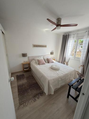 a white bedroom with a bed and a ceiling fan at La Guapa in Cala en Porter