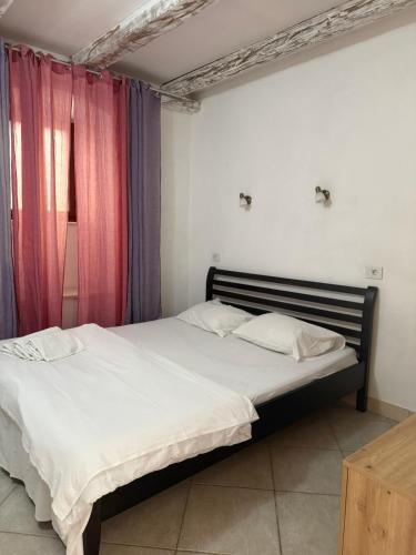 a bedroom with a bed with white sheets and pink curtains at Apartman Perast in Perast