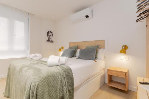 a white bedroom with a bed with a green blanket at Pension Txapitela in Pamplona