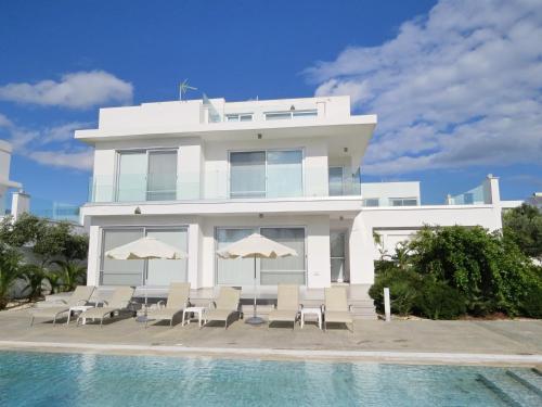 a white building with chairs and umbrellas next to a swimming pool at Royal Sugar in Ayia Napa