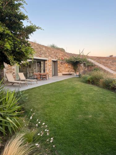 a garden with chairs and a table and a brick building at On The Rocks - The Pebbles - Serviced Villas in Ios Chora