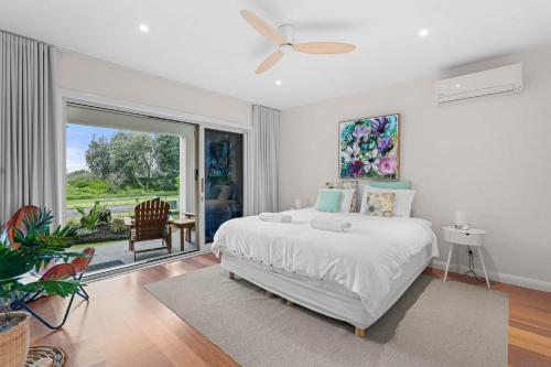 a white bedroom with a bed and a large window at Werri Big Beach House in Gerringong