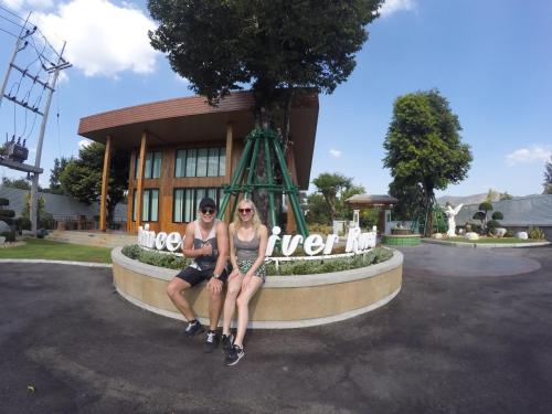 two women sitting on a sign in front of a building at Princess River Kwai Hotel in Kanchanaburi