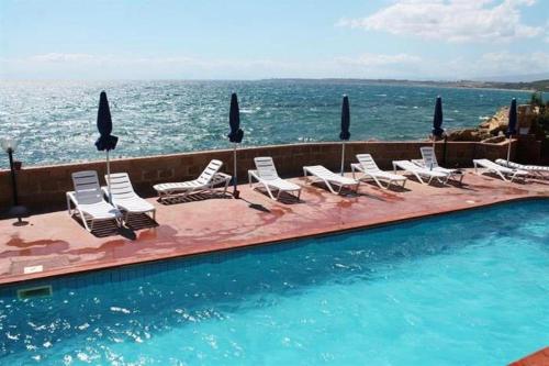 a group of chairs and a swimming pool with the ocean at Cala Longa Poseidon Beach Resort in Casa dello Stumio