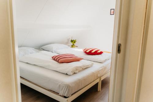a bed with white sheets and red pillows on it at Vakantiehuis dicht bij het strand in Ouddorp