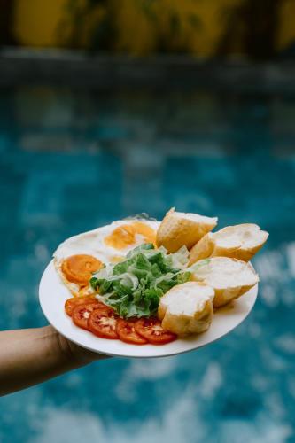 a person holding a plate of food with tomatoes and chips at Tam Coc Mango Homestay - Free Swimming Pool in Ninh Binh